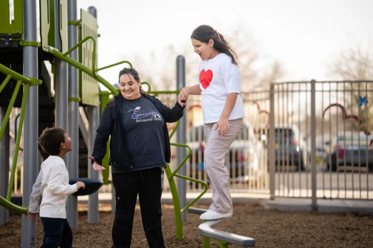 Children playing on playground equipment with an adult supervising and helping one child balance