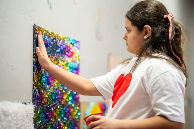 Niña tocando una obra de arte colorida con lentejuelas en una pared