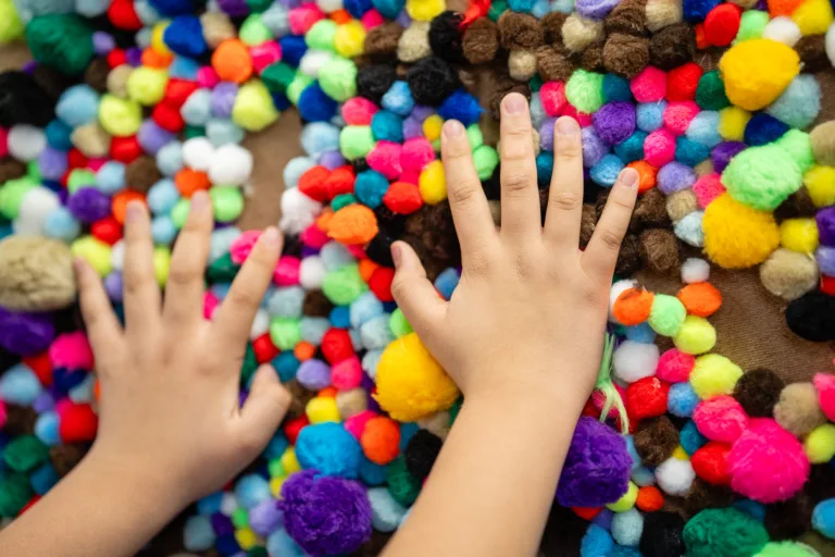 Manos de niños tocando una superficie de manualidades con pompones coloridos