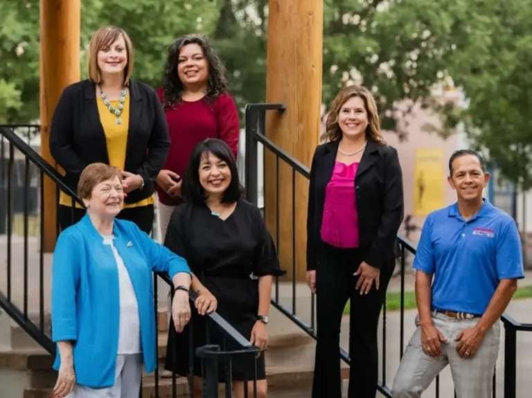 Group portrait of six adults standing on outdoor steps by wooden posts and black railings