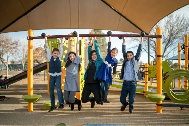Four children hanging from a playground monkey bar under a canopy