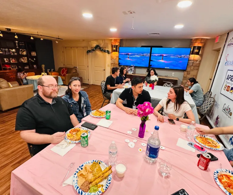 People seated around a table at a casual indoor gathering, eating and talking in a lounge-like room