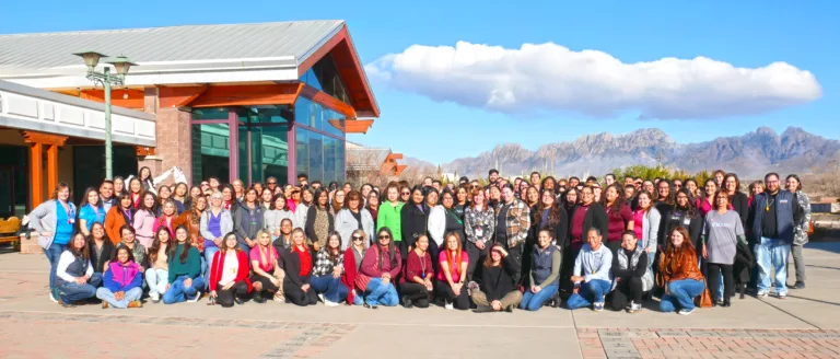 Large group posing for a photo outside a building with mountains in the background