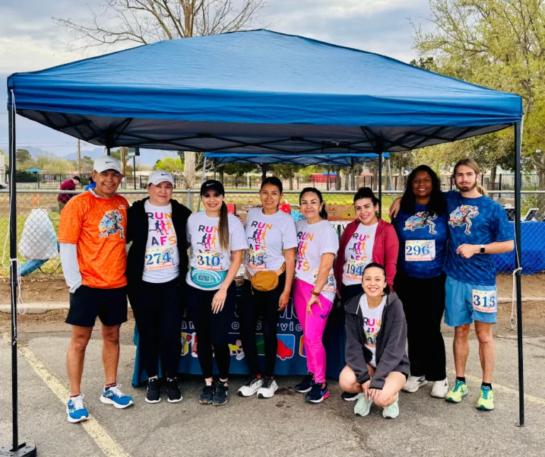 Group of runners posing under a blue canopy at a race event