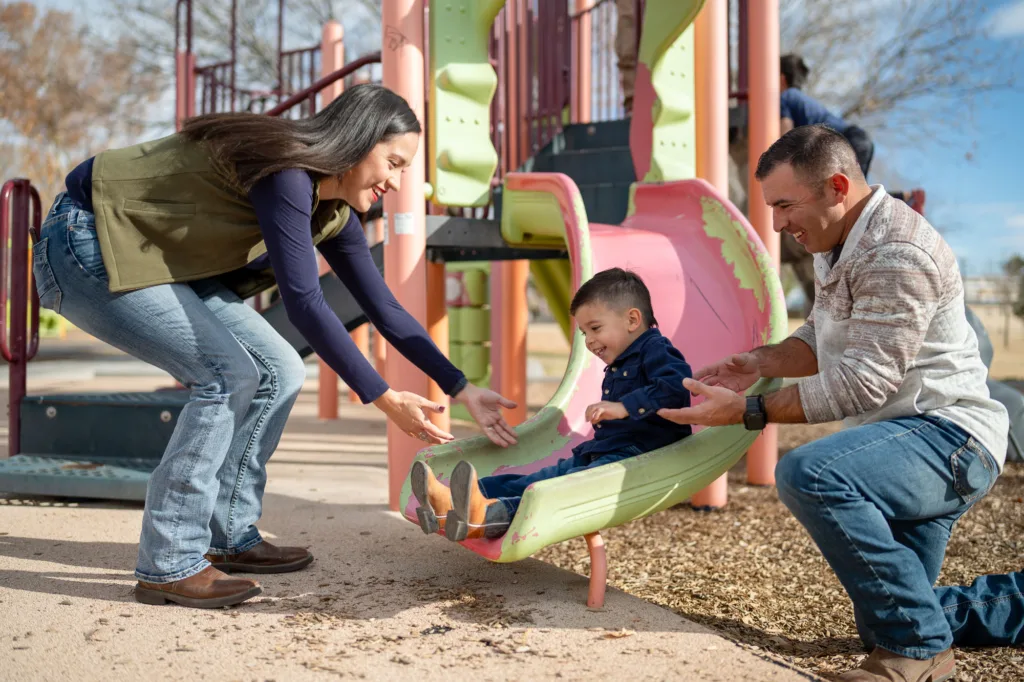 Padres ayudando a un niño pequeño en un tobogán de un parque infantil