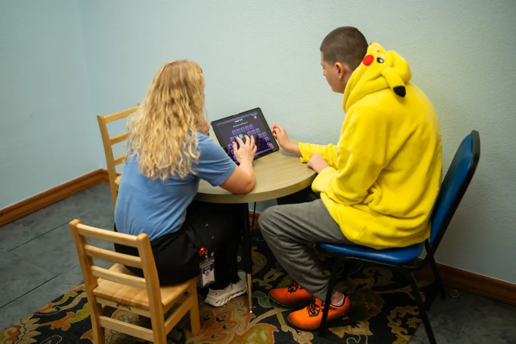A child and a therapist sit together during a tablet activity.