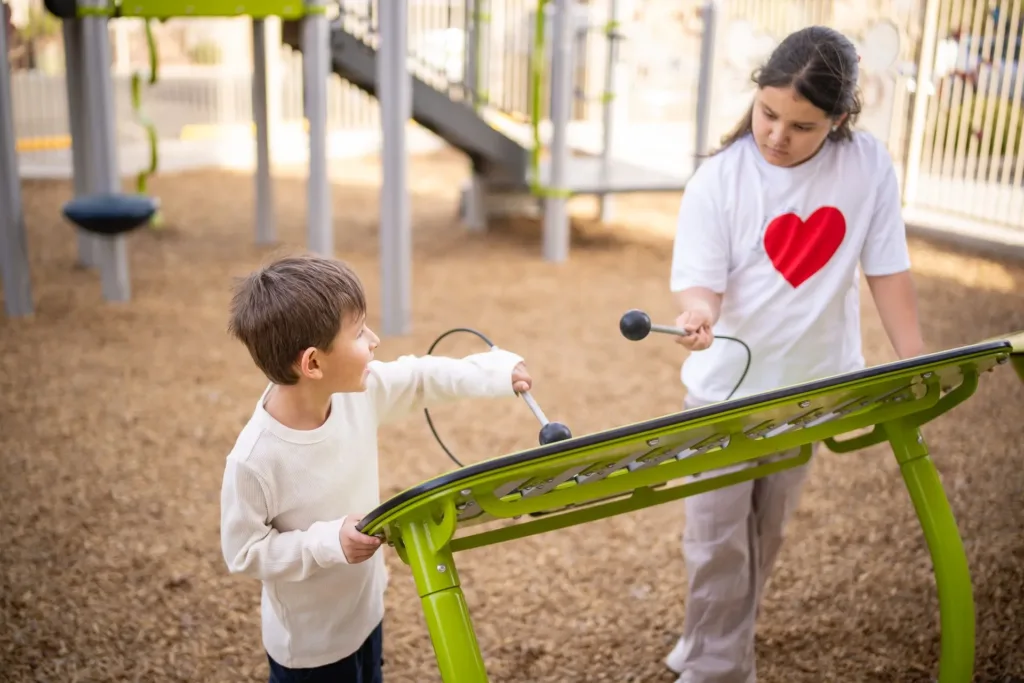 Dos niños tocando un instrumento musical verde en un parque infantil.