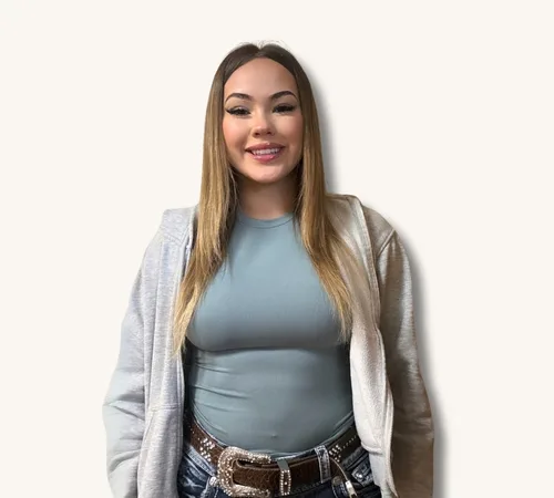 Allie Espinosa standing against a plain background, wearing a gray hoodie over a blue top and jeans