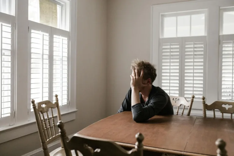 A person sitting alone at a dining table with their hand on their face, feelings of anxiety.