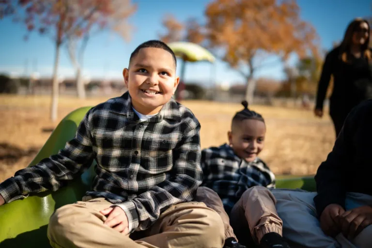 Dos niños sonriendo al aire libre, sentados juntos al sol.