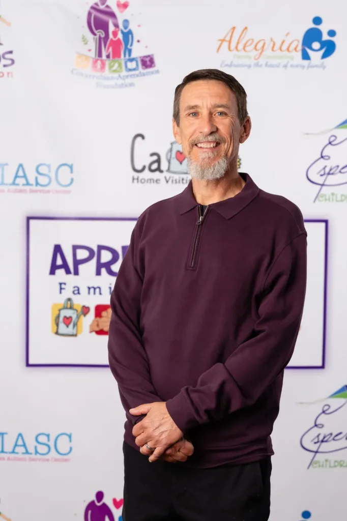 Dean Palma smiling and standing in front of an Aprendamos Family of Services event backdrop.
