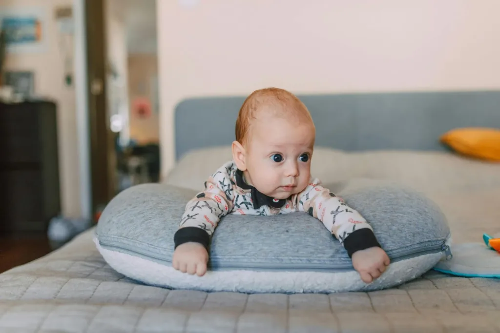 Baby on gray pillow, looking off to the side on a bed.