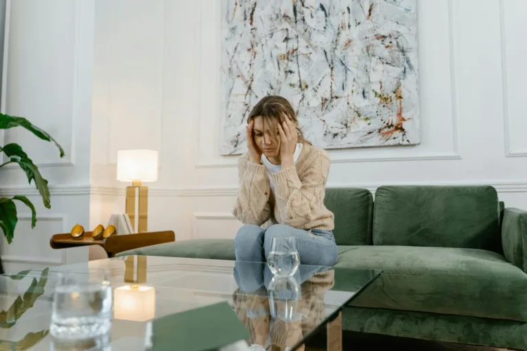 Woman with hands on head sits on green couch, looking stressed; living room setting.
