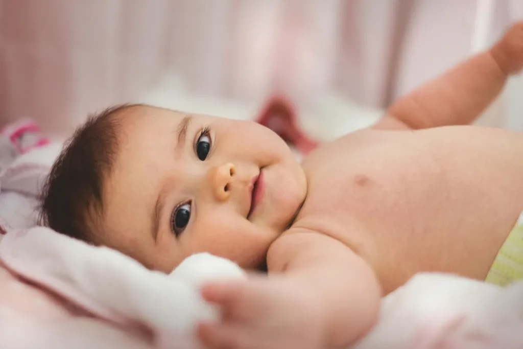 Baby lying on a soft blanket, looking at the camera and smiling.