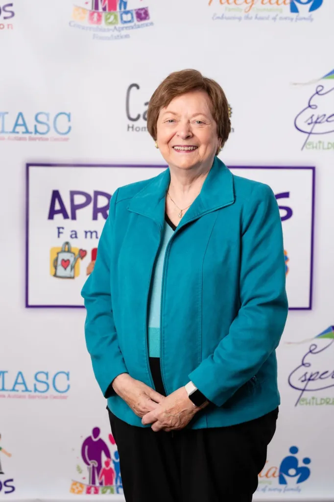 Woman in blue jacket standing in front of a banner with text and logos, smiling.