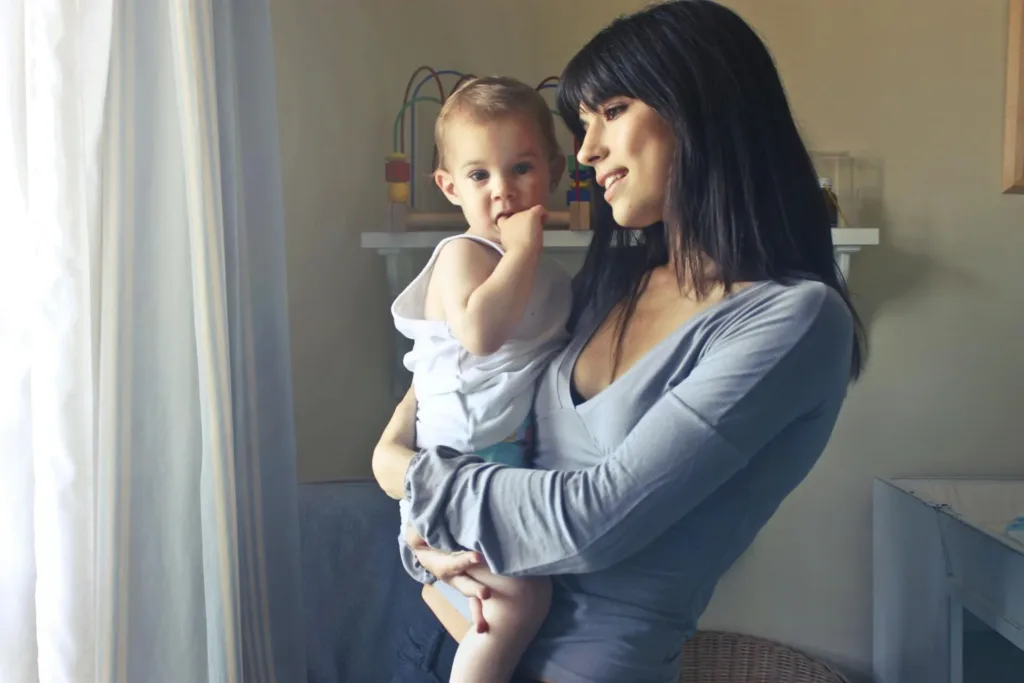 Woman holding a baby near a window, both looking towards the light.