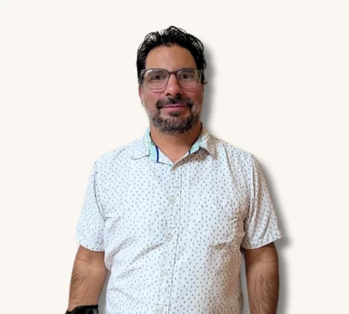 Josh Tafoya standing against a plain light background, wearing glasses and a white patterned shirt