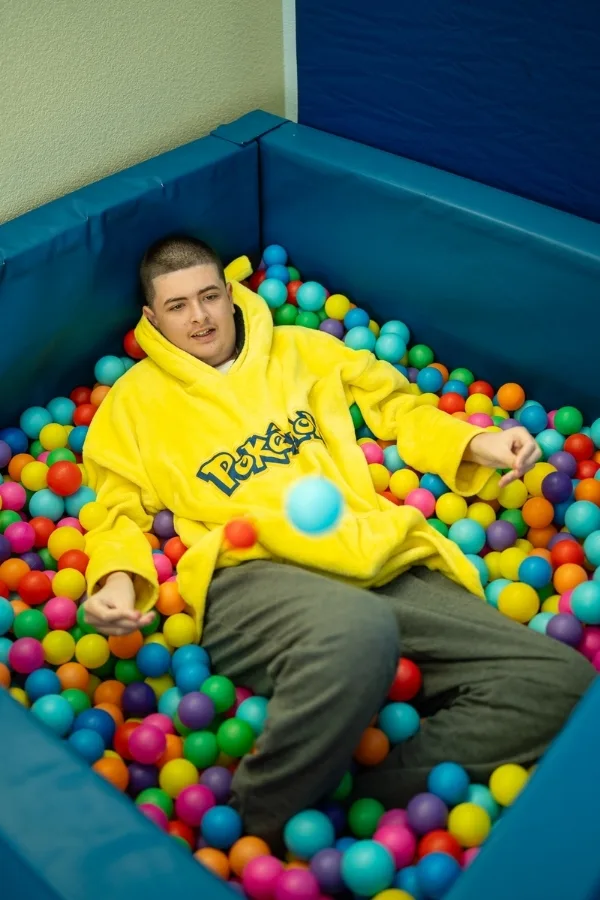 Teenager relaxing in a ball pit wearing a yellow Pokémon hoodie