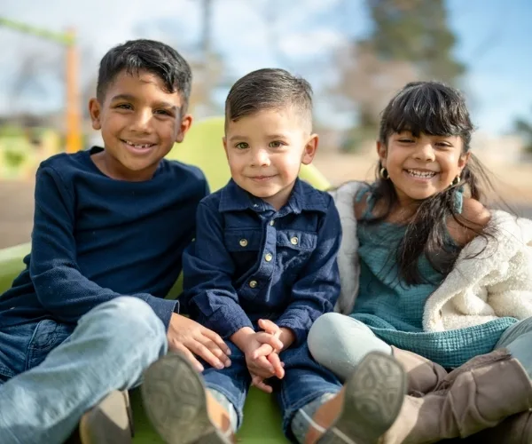 Three children sitting together and smiling outdoors
