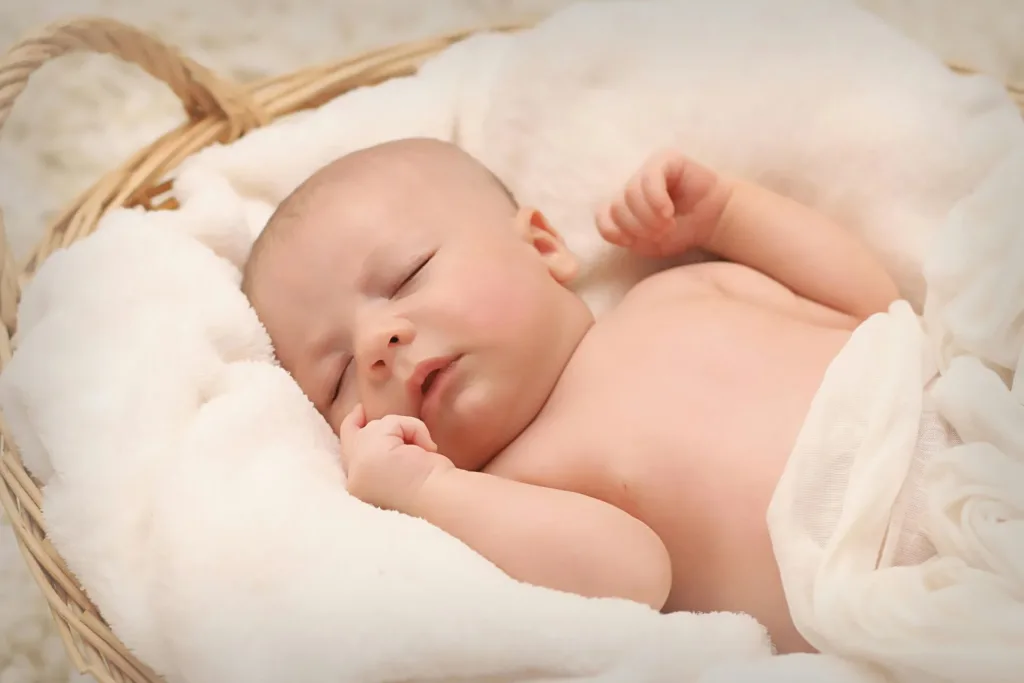Baby sleeping peacefully in a basket lined with soft, white fabric.
