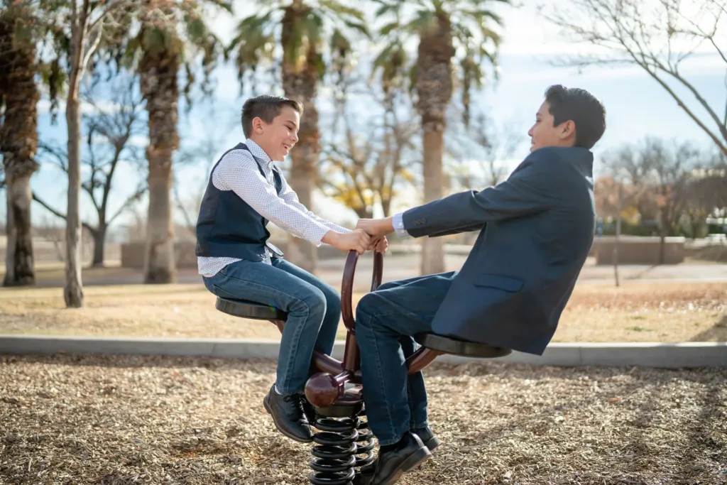 Two boys play on a spring rider in a park, holding hands.