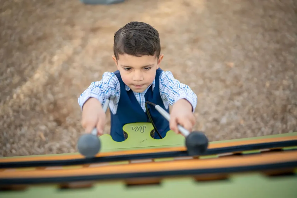 Boy playing outdoor xylophone with mallets.