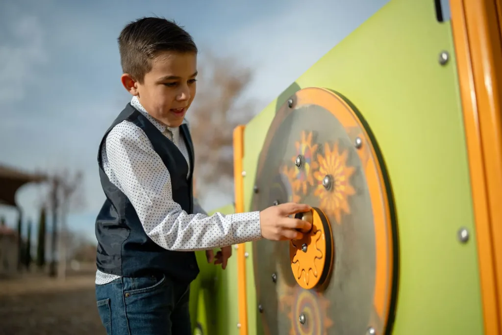 A young boy engages with a sensory play panel outdoors, practicing motor skills and focus.