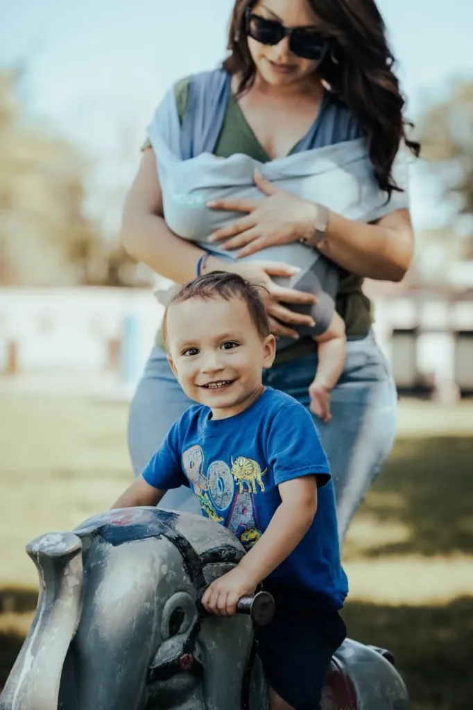 Smiling toddler in a blue shirt sitting on a park bench, with mom after receiving Early Intervention