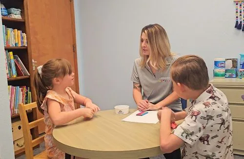 Therapist sitting with two children during a play-based counseling activity at a table