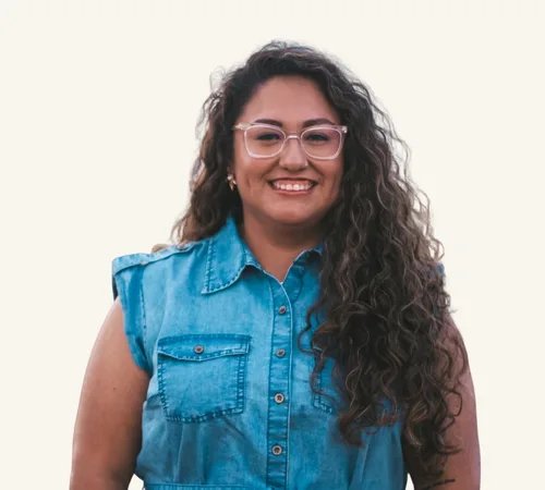 Smiling woman with long curly hair wearing glasses and a sleeveless denim shirt